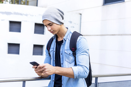Typing text message. Side view of handsome young man in smart casual wear holding mobile phone while leaning at a benchの写真素材