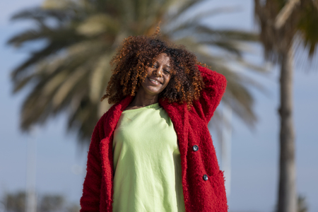 Front view of young beautiful curly woman standing on path smiling while looking camera in sunny dayの写真素材