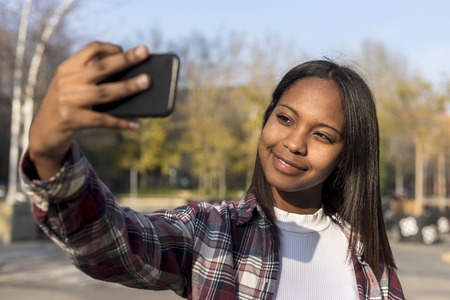 Young african american woman standing outdoors while taking a selfie in sunny dayの写真素材