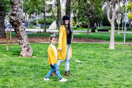 Beautiful happy young mother walking with her daughter, both smiling and looking into the camera, park in backgroundの写真素材
