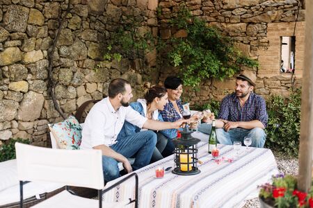 Portrait of happy young people sitting together and laughing while enjoying at a party with cocktails on table.の写真素材