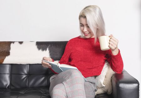 Caucasian woman sitting on sofa drinking coffee and reading book