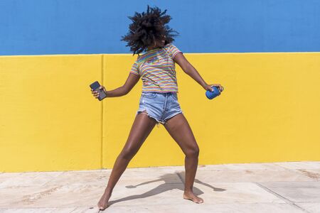 Mixed race smiling black woman portrait with big afro curly hair against blue and yellow wall...