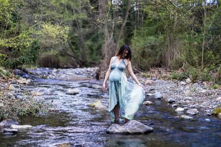Beautiful pregnant girl posing near the river wearing a green dress.の写真素材