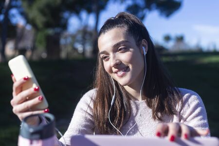 Beautiful girl sitting on a bench brunette in a casual clothe, fashion life style with a phone....