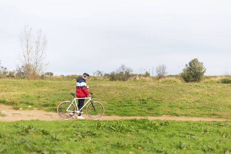 Young man enjoying a bicycle ride and using a smartphone while walking on parkの写真素材