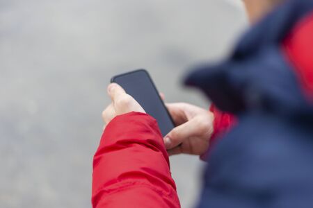 Young man with smartphone in hand texting outside in the street