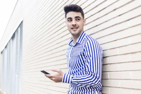 Young man leaning on house wall while using his smartphoneの写真素材