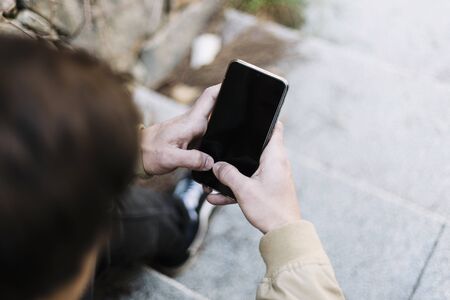 Rear view of a hispanic young man using mobile phone while sitting outdoorsの写真素材