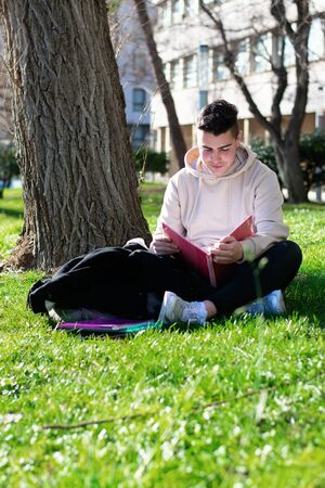Teenager sitting on the school grass while studying with a bookの写真素材