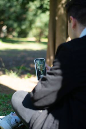 Back view of a young teenager student sitting on campus while using a mobile phone