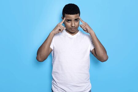 Horizontal portrait of black male in white t-shirt with fingers on temples, isolated on blue...