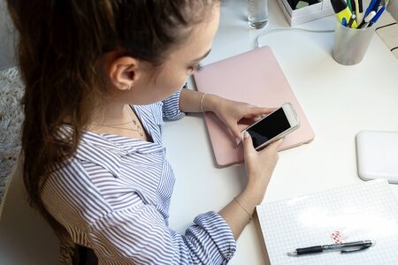 Young girl sitting at a laptop and using a smartphone.