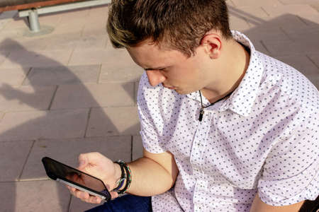 Young man using mobile phone while sitting outdoorsの写真素材