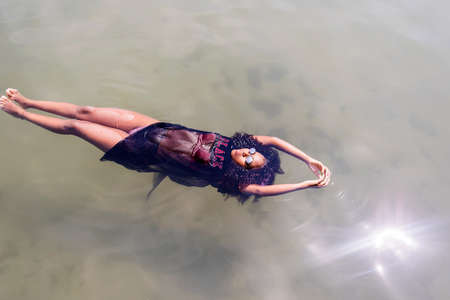 Beautiful young African American woman floating in a pool of waterの写真素材