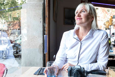 Beautiful blonde woman sitting in a cafe while looking away and she has a camera on the table.