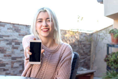 Young woman holding out a cellphone in her handの写真素材