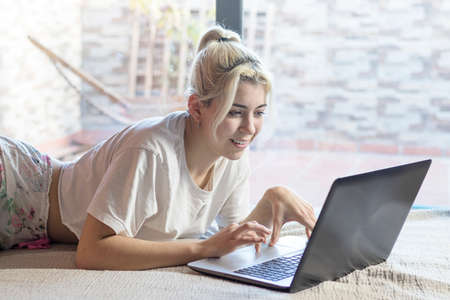 Smiling girl using a laptop while lying on her bed