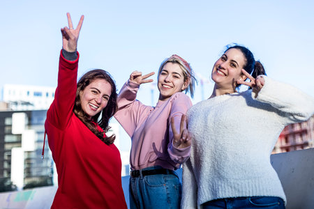 Front view of three young Teenage girls making a peace sign outdoors in a sunny dayの写真素材
