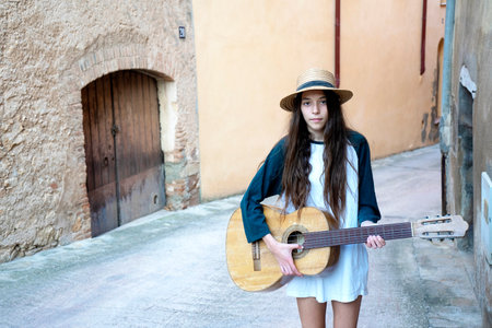 Female young musician in summer clothes on walking on antique street while playing acoustic guitar.の写真素材