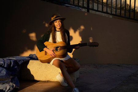 Female young musician in summer clothes on antique stoned bench playing acoustic guitar.の写真素材