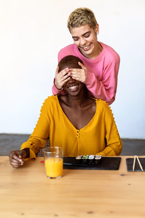 Girl surprising her female best friend. Model covering her eyes and hugging from behind. Two surprised girls. Women having fun and showing face emotionsの写真素材