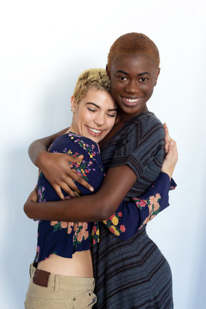 Photo of joyful ladies embrace and enjoy togetherness, being of different of races, dressed in casual jumpers, isolated over white background. Diverse women laugh happily, have fun together.の写真素材
