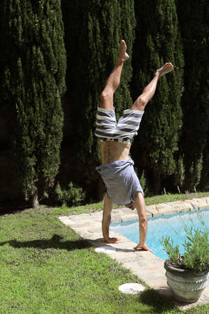 Male wearing t-shirt and swimsuit doing a handstand on poolside