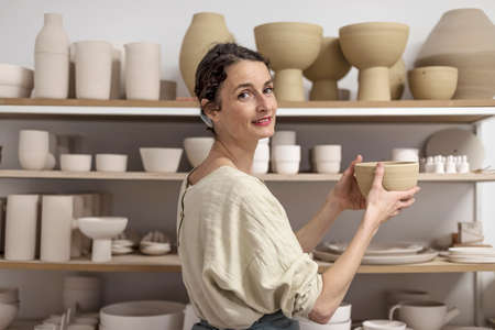 Young female ceramist indoors holding handmade clay product. Conception of potteryの写真素材