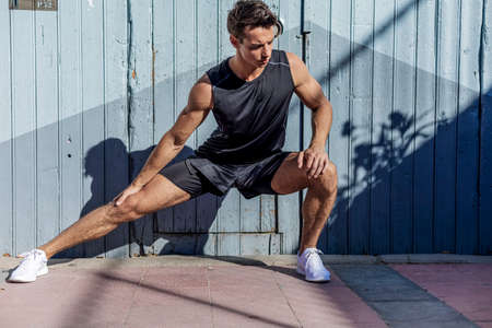 Man runner stretching legs preparing for run training doing warm-up