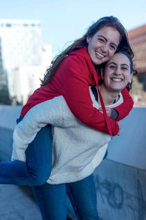 Half length of two blonde and redhead women friends having fun outdoor in the city, riding piggyback - happiness, friendship, having fun conceptの写真素材