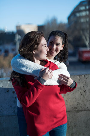 Close-up photo of laughing woman friends hugging each other on city streetの写真素材