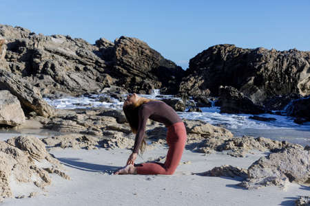Young woman practice balance asanas on Summer yoga session on a beautiful beach at Formentera,...