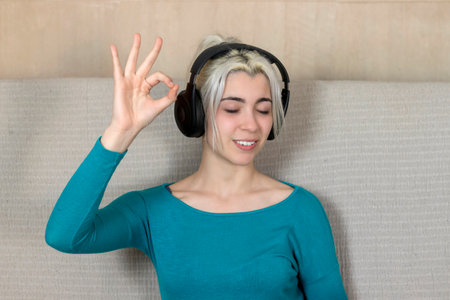 A Woman closed eye and enjoying the music and relax sit at home, making Ok gestureの写真素材
