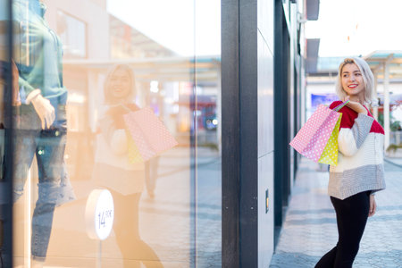 Blonde smiling woman holding shopping bags while standing next to a shopping mallの写真素材