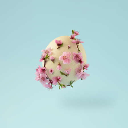 Easter flying ostrich egg with colorful flowers on a bright blue background. Minimal spring concept.