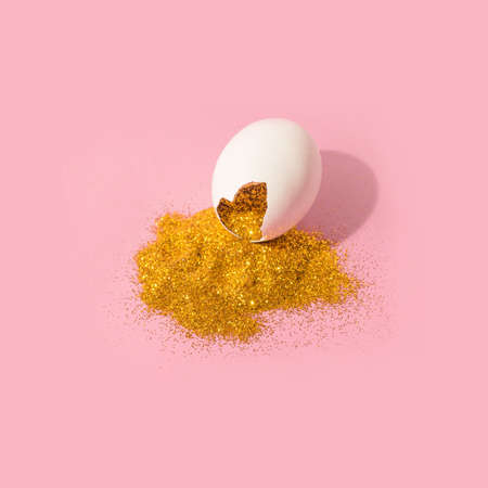 Eggshell with gold glitter. Creative copy space on pink pastel background. Minimal Easter holiday...