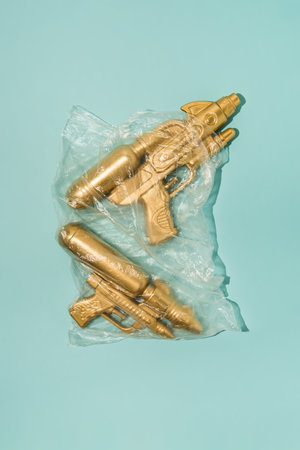 Golden water-gun wrapped in transparent plastic bag on pastel blue background. Creative summer...