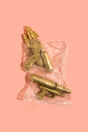 Set of two Gold Waterguns in plastic transparent bag against powder pink background. Summer colorful concept. Minimal, flat lay.の写真素材