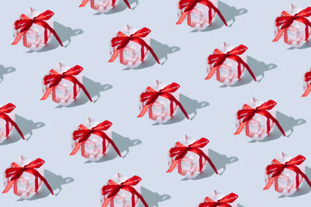 Pattern made of christmas gift box on blue bright background. Minimal New year creative idea with ice cube and red ribbon decoration. Authentic presents in isometric composition.の写真素材