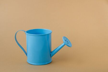 Toy blue watering can against a light brown background.の写真素材