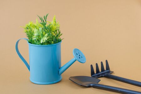 Toy watering can purple blue with yellow-green sprigs, rakes and shovel on a grey brown background. Place for text. Agriculture concept.の写真素材