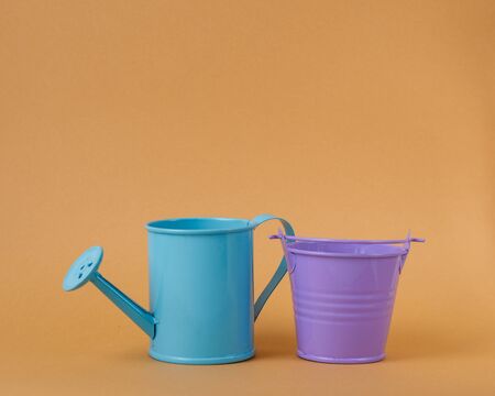 Toy iron blue watering can and purple bucket on an orange background. Place for text. Agriculture concept.の写真素材