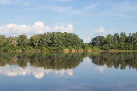 Summer. Blue sky, white clouds and green bank are reflected in the river.の写真素材