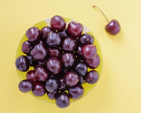 Red sweet cherry in a yellow cup and one single berry on a beige background. View from above.の写真素材