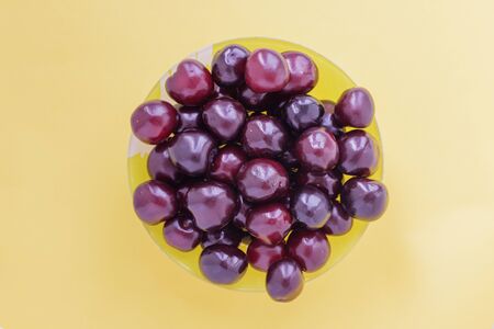 Red sweet cherry in a yellow cup on a beige background. View from above.の写真素材