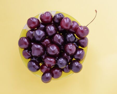 Red sweet cherry in a yellow cup on a beige background. View from above.の写真素材