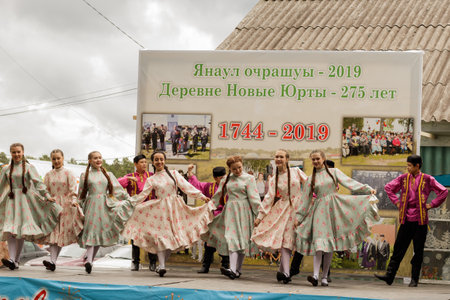 Aromashevo, Russia, July 6, 2019. Teenagers in traditional Tatar clothes dance on stage against the backdrop of a stand with historical photographs. Feast of the Siberian village of New Yurts.のeditorial素材