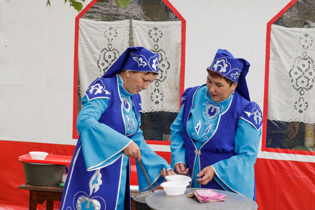 Aromashevo, Russia, July 6, 2019. Two women in national Tatar clothes pours soup into plates for guests of the holiday. Day of the Siberian village of New Yurts.のeditorial素材