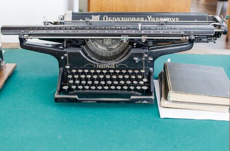 An Underwood typewriter with Russian letters on a tabletop covered with green fabric. Near old books. Inscription Model Underwoodの写真素材